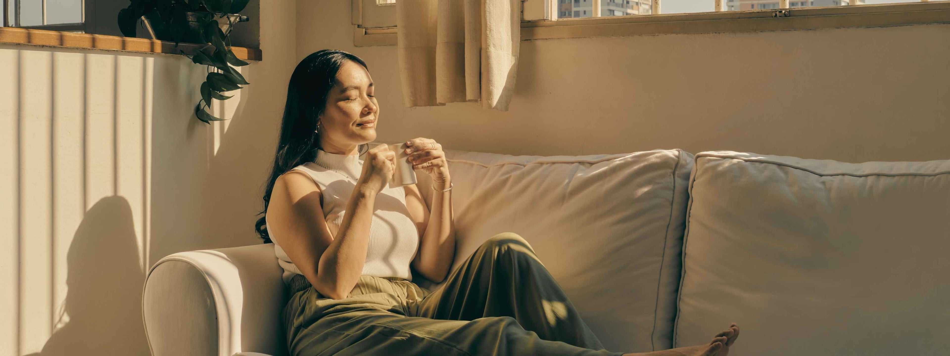 Peaceful woman sitting mindfully on a couch, holding a cup of tea and enjoying a calm moment of self-care