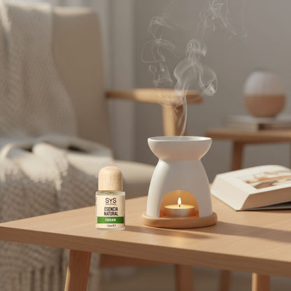 Aromatherapy diffuser with a candle and cedar essential oil bottle on a wooden table in a cozy living room.