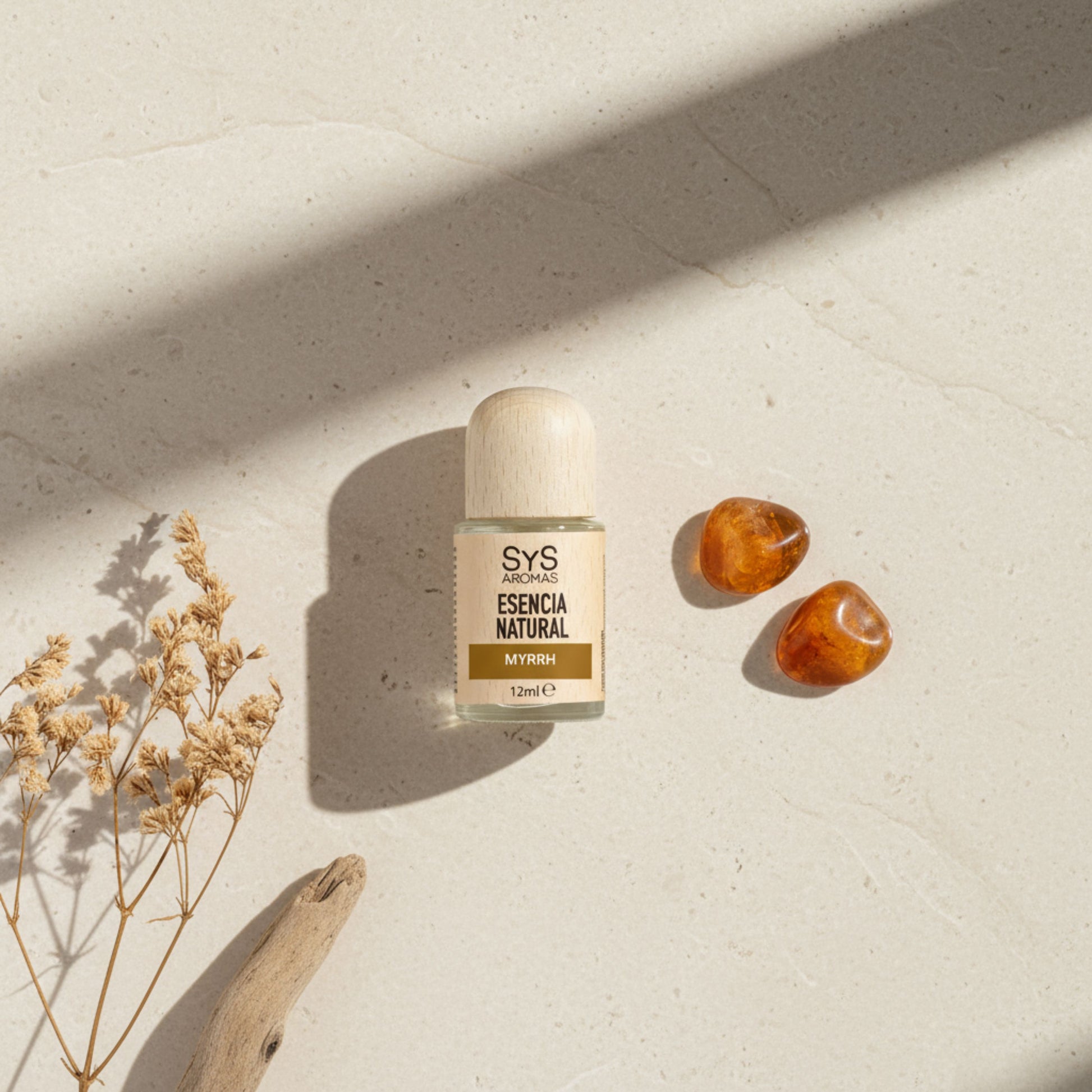 Myrrh essentail oil on a beige surface with dried plants and amber stones.