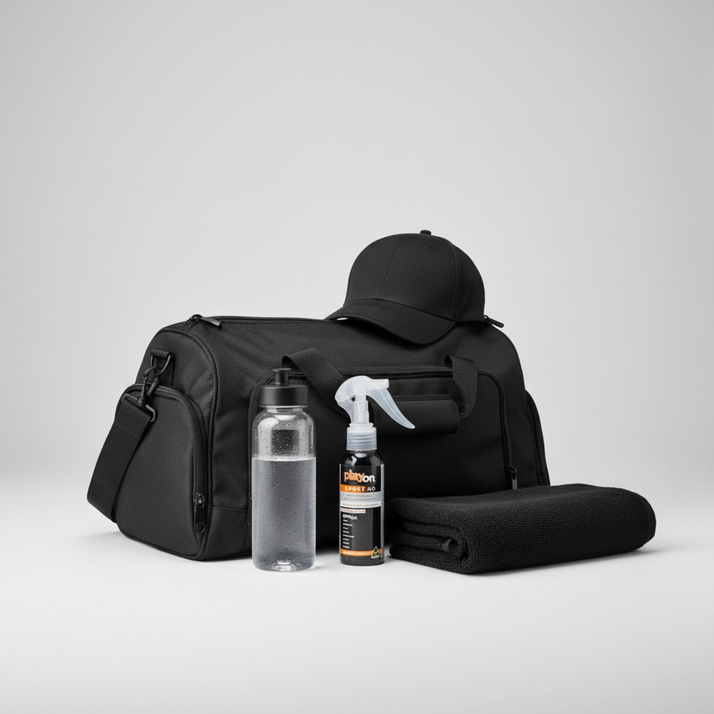 Black duffel bag with a cap, water bottle, towel and playon spray 80ml on a light grey background.