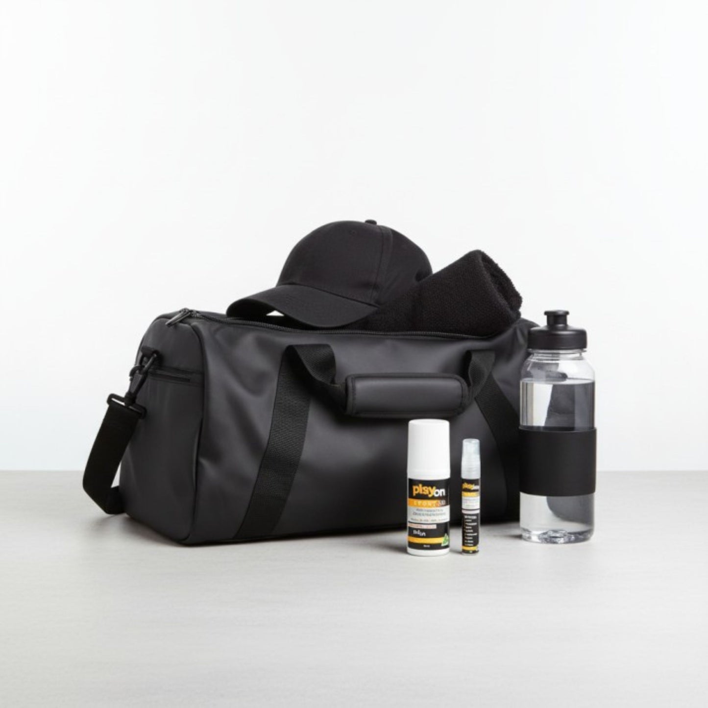 Black duffel bag with a cap, bottles, and playon travel pack - playon roll on and playon mini on a light grey background.