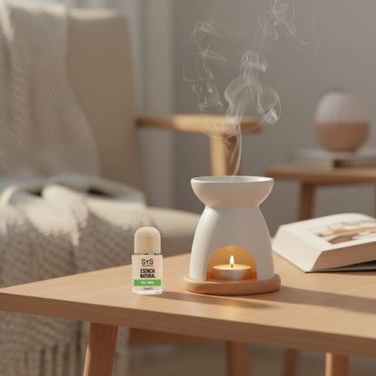 White essential oil burner with a candle and tea tree oil 12ml on a wooden table, surrounded by a cozy living room setting.