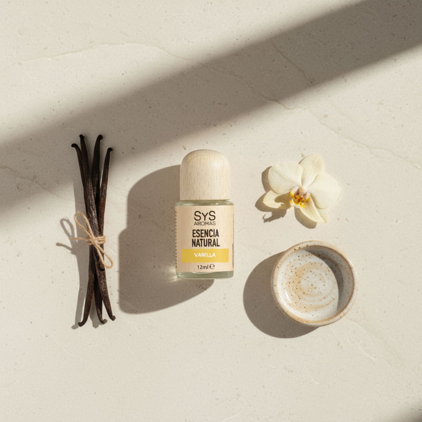 Vanilla essential oil with with vanilla beans and a flower on a light surface